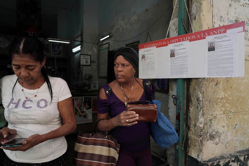 Mujeres salen de una tienda estatal subvencionada, o "bodega", junto a un cartel que anuncia a los candidatos para las próximas elecciones legislativas en el centro de La Habana