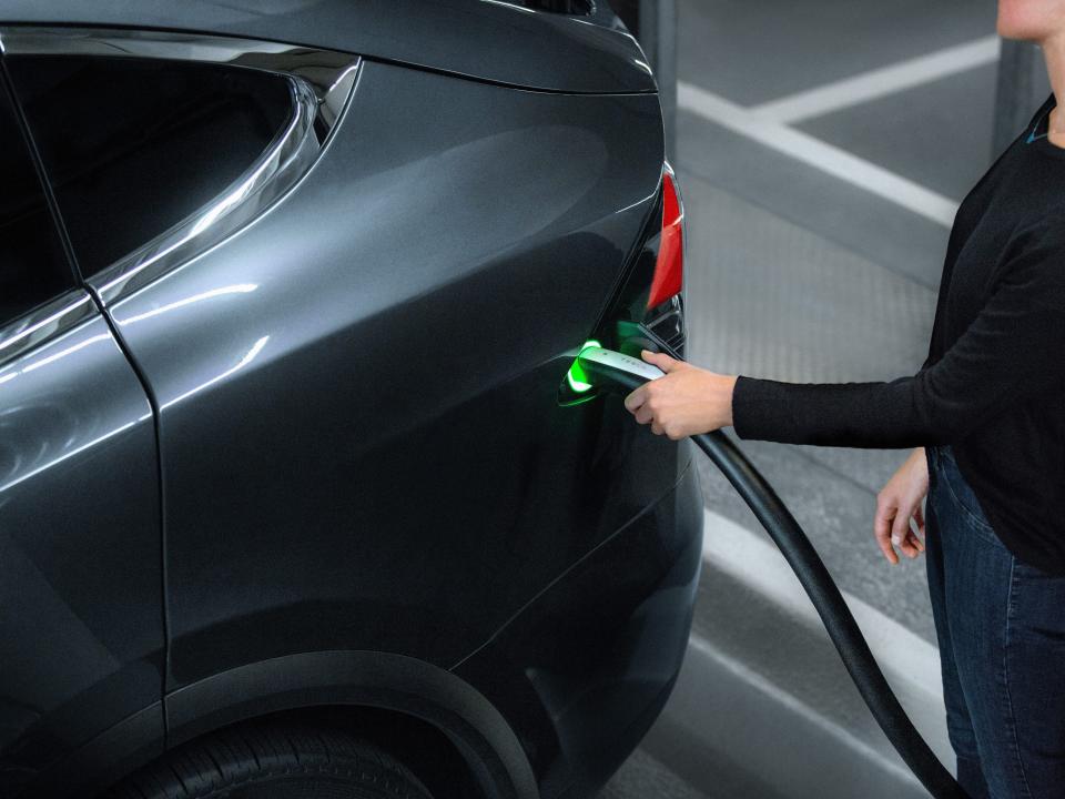 A woman plugs an EV charger into a dark-colored Tesla.