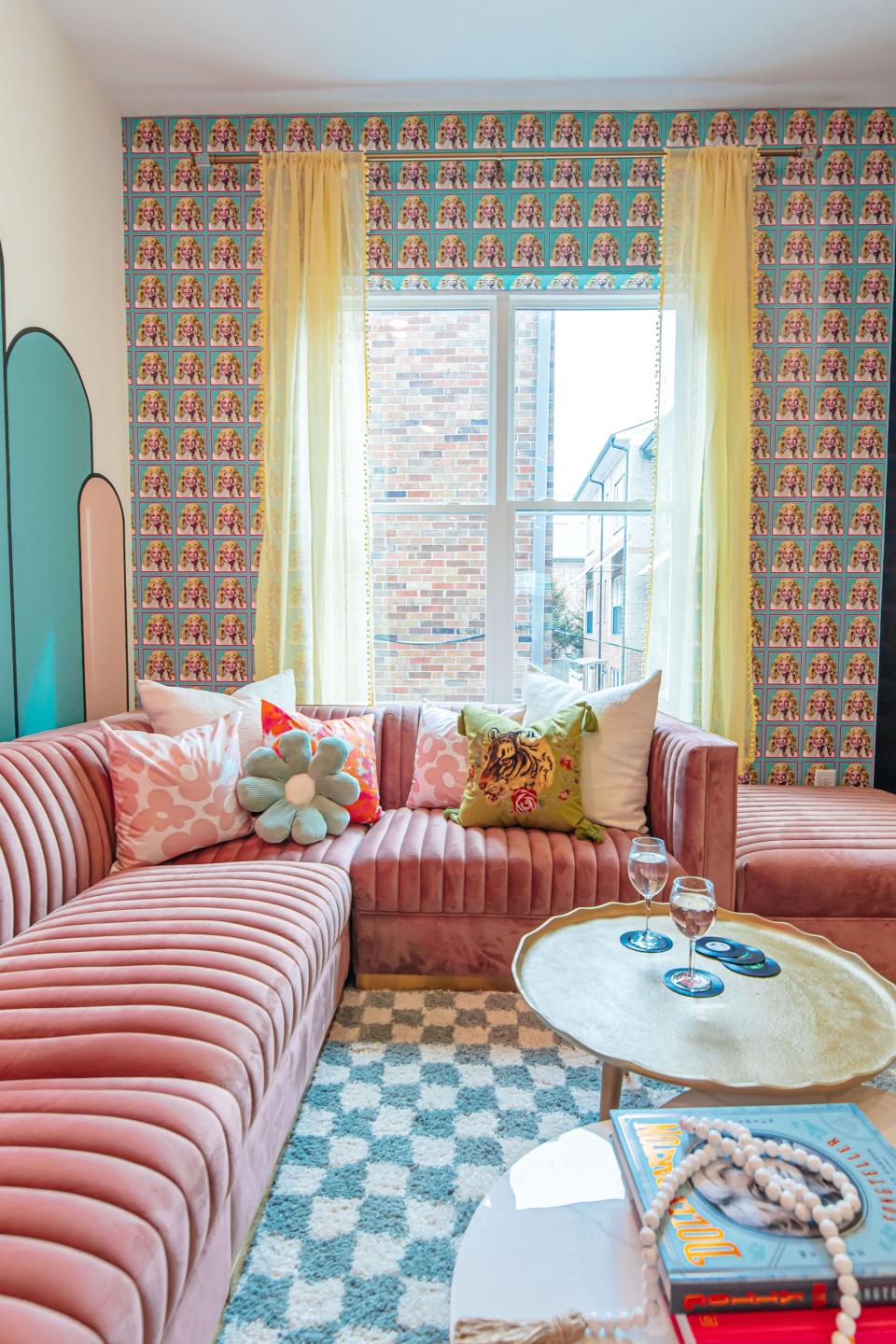 A colorful living room with a pink couch, two coffee tables, and a printed wallpaper.