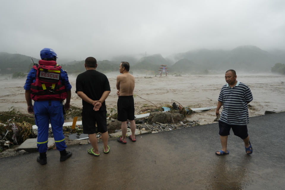 A rescue worker and other residents look out over an overflowing river in the Miaofengshan area on the outskirts of Beijing, Tuesday, Aug. 1, 2023. Chinese state media report some have died and others are missing amid flooding in the mountains surrounding the capital Beijing. (AP Photo/Ng Han Guan)