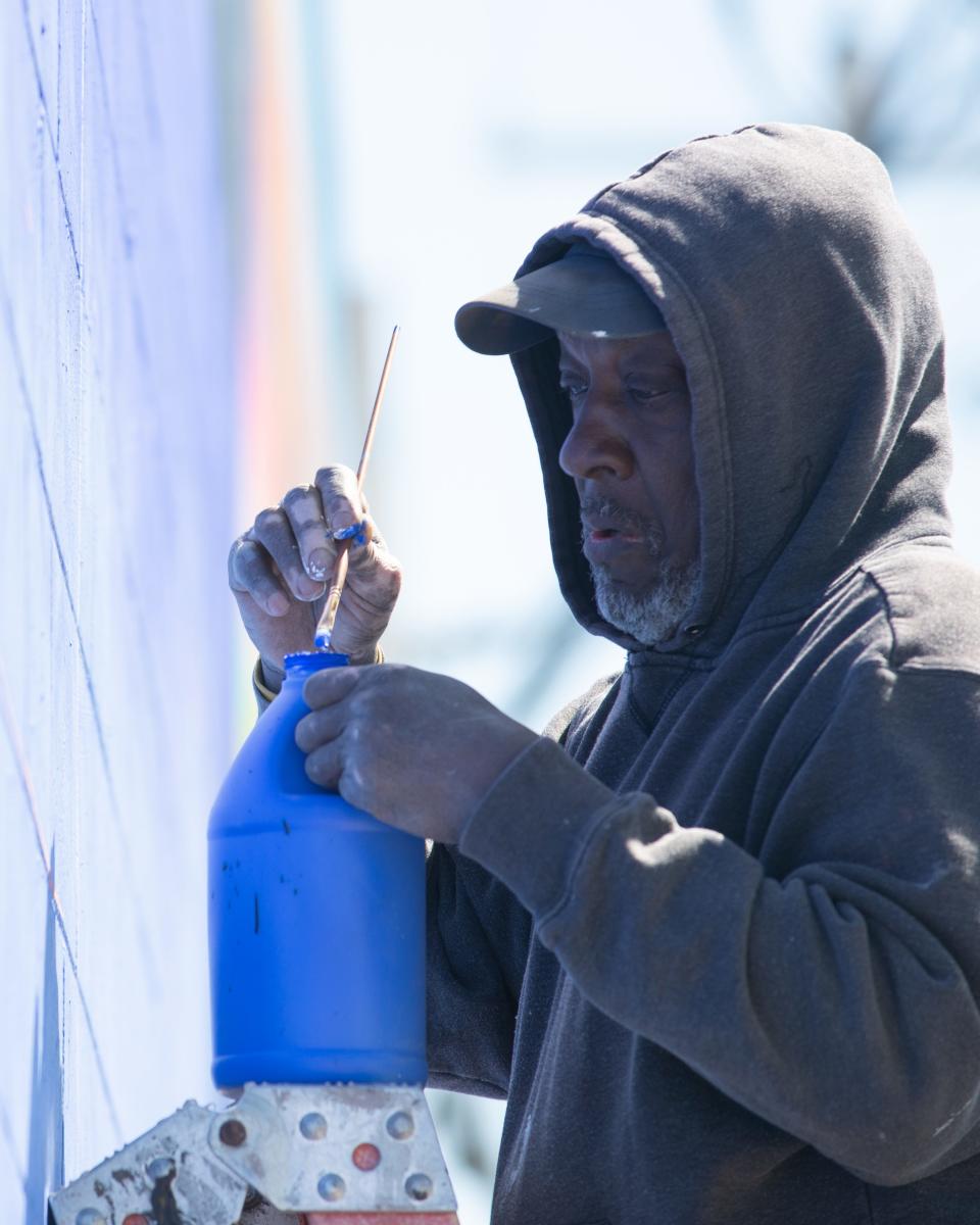 George Mayfield uses a thin paintbrush to outline details on his portion of the multicultural mural.