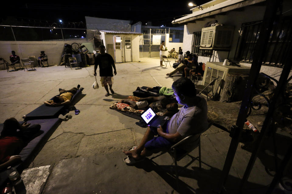 In this July 25, 2019, photo, a Cuban man looks at a computer screen as others lay around the patio at El Buen Pastor shelter for migrants in Cuidad Juarez, Mexico. (AP Photo/Gregory Bull)