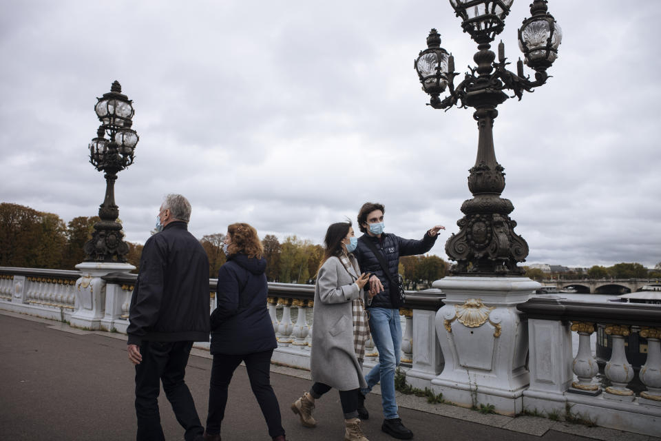 People wearing masks, walk on Alexandre III bridge in Paris, Sunday Oct.25, 2020. A curfew intended to curb the spiraling spread of the coronavirus, has been imposed in many regions of France including Paris and its suburbs. (AP Photo/Lewis Joly)