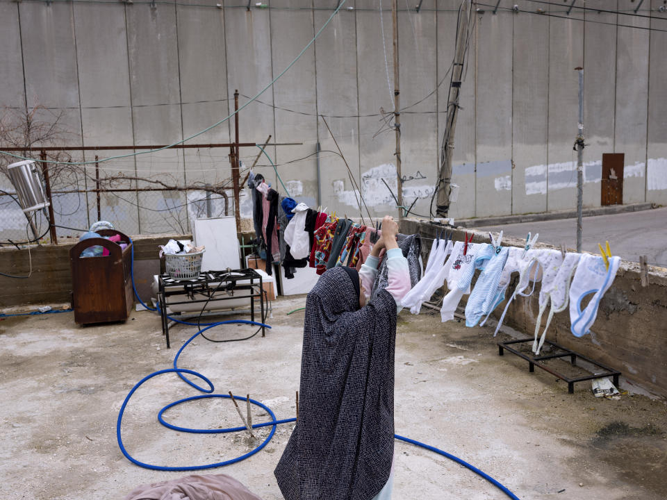 FILE - A Palestinian hangs laundry at her house located next to Israel's separation barrier in the West Bank village of Abu Dis in the outskirts of Jerusalem, Jan. 31, 2022. (AP Photo/Oded Balilty, File)