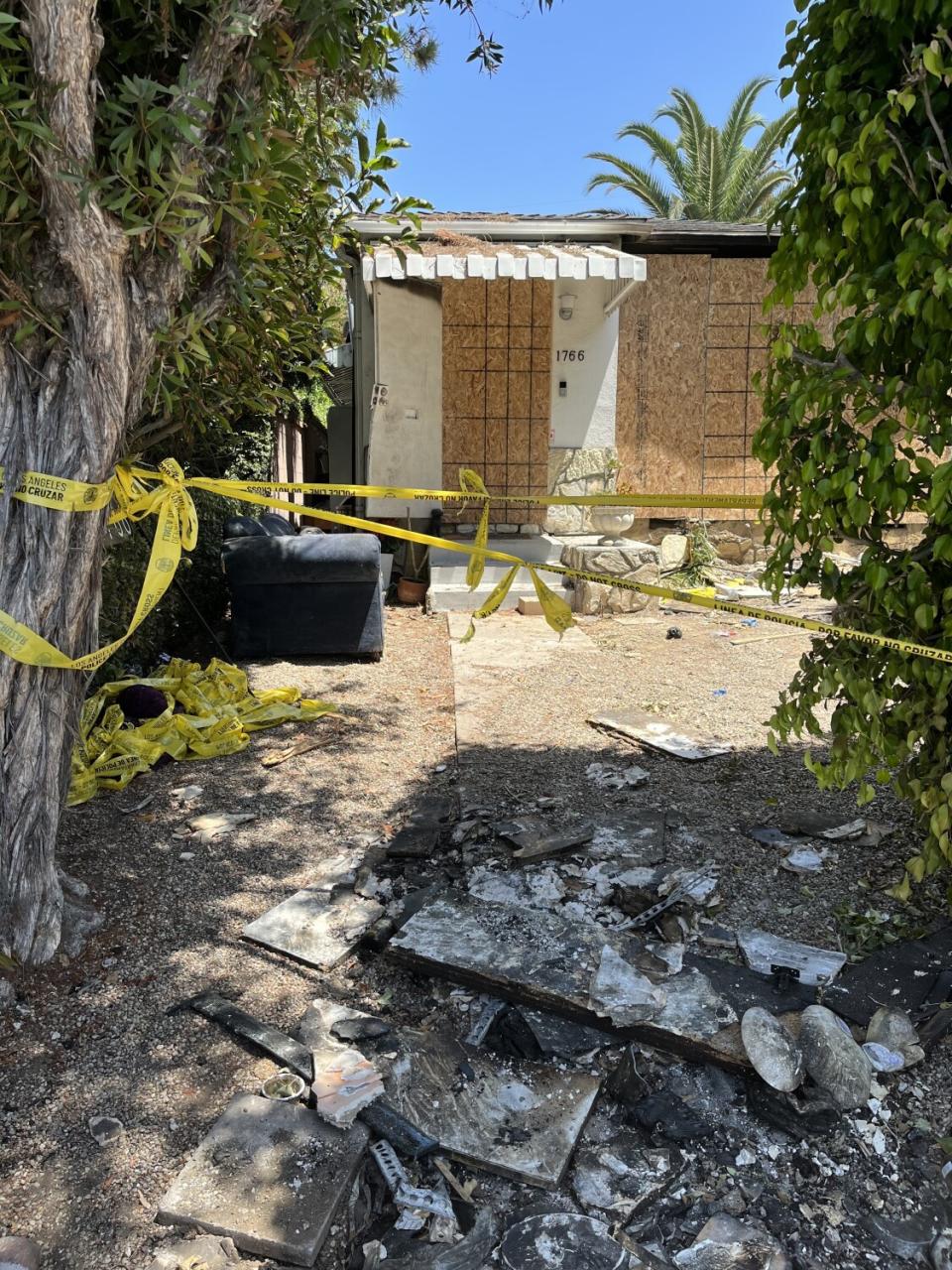 Police tape in front of a damaged home boarded up with plywood