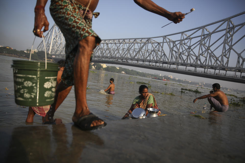 A man carries a bucket of water while people wash utensils, brush their teeth and bathe in the polluted waters of the river Hooghly, a distributary of the river Ganges and known as Ganga by locals, in the backdrop of the landmark Howrah Bridge in Kolkata, in the eastern Indian state of West Bengal, Friday, October 11, 2019. Once the capital of the British raj, today the seething metropolis is home to nearly 15 million people. (AP Photo/Altaf Qadri)