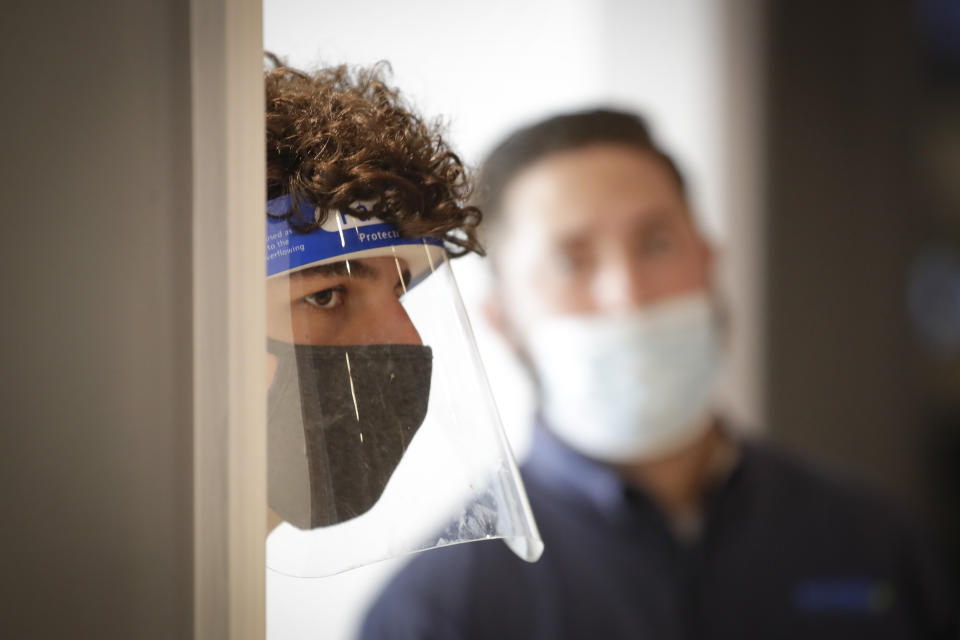 A host wears a face shield as he waits to sit customers at Slater's 50/50 Wednesday, July 1, 2020, in Santa Clarita, Calif. California Gov. Gavin Newsom has ordered a three-week closure of bars, indoor dining and indoor operations of several other types of businesses in various counties, including Los Angeles, as the state deals with increasing coronavirus cases and hospitalizations. (AP Photo/Marcio Jose Sanchez)