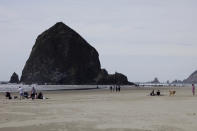 This Thursday, May 28, 2020, photo shows people visiting a beach in front of Haystock Rock during the coronavirus outbreak in Cannon Beach, Ore. With summer looming, Cannon Beach and thousands of other small, tourist-dependent towns nationwide are struggling to balance fears of contagion with their economic survival in what could be a make-or-break summer. (AP Photo/Gillian Flaccus)