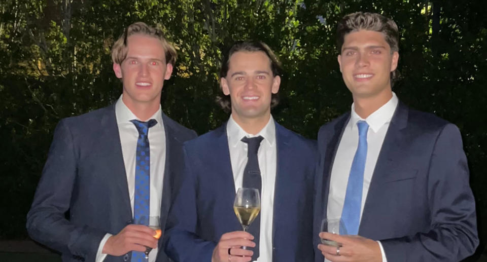 Three men in blue suits and ties holding drinks and smiling. 