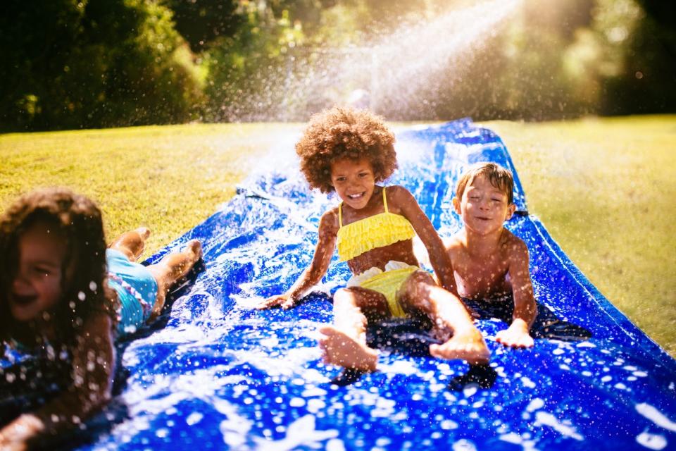 Laughing girl and friends playing together on a water slide in their yard in the sun.