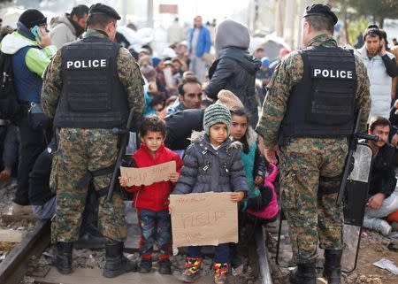 Migrants' children stand among police officers as their families wait to cross the border from Greece into Macedonia, near Gevgelija, Macedonia November 24, 2015. REUTERS/Stoyan Nenov