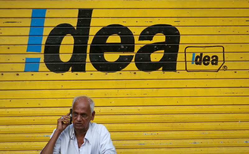 FILE PHOTO: A man speaks on his mobile phone as he sits in front of a shop displaying the Idea Cellular Ltd's logo on its shutter in Mumbai