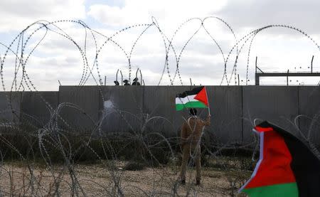 A protester holds a Palestinian flag in front of Israeli troops during clashes at a protest marking the 12th anniversary of a campaign against the Israeli barrier, in the West Bank village of Bilin near Ramallah February 17, 2017. REUTERS/Mohamad Torokman