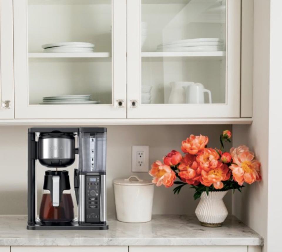 Ninja coffee machine on the kitchen counter near a canister and vase of flowers. 