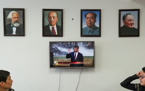 Framed portraits of German philosopher Karl Marx, Soviet state founder Vladimir Lenin and China's late leaders Mao Zedong and Deng Xiaoping hung above a screen showing a news broadcast of China's President Xi Jinping - Credit: Reuters 