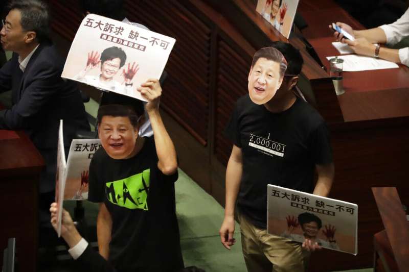 香港泛民主派議員在立法會議場戴起習近平面具，拿著林鄭月娥的看板表達不滿。（美聯社）