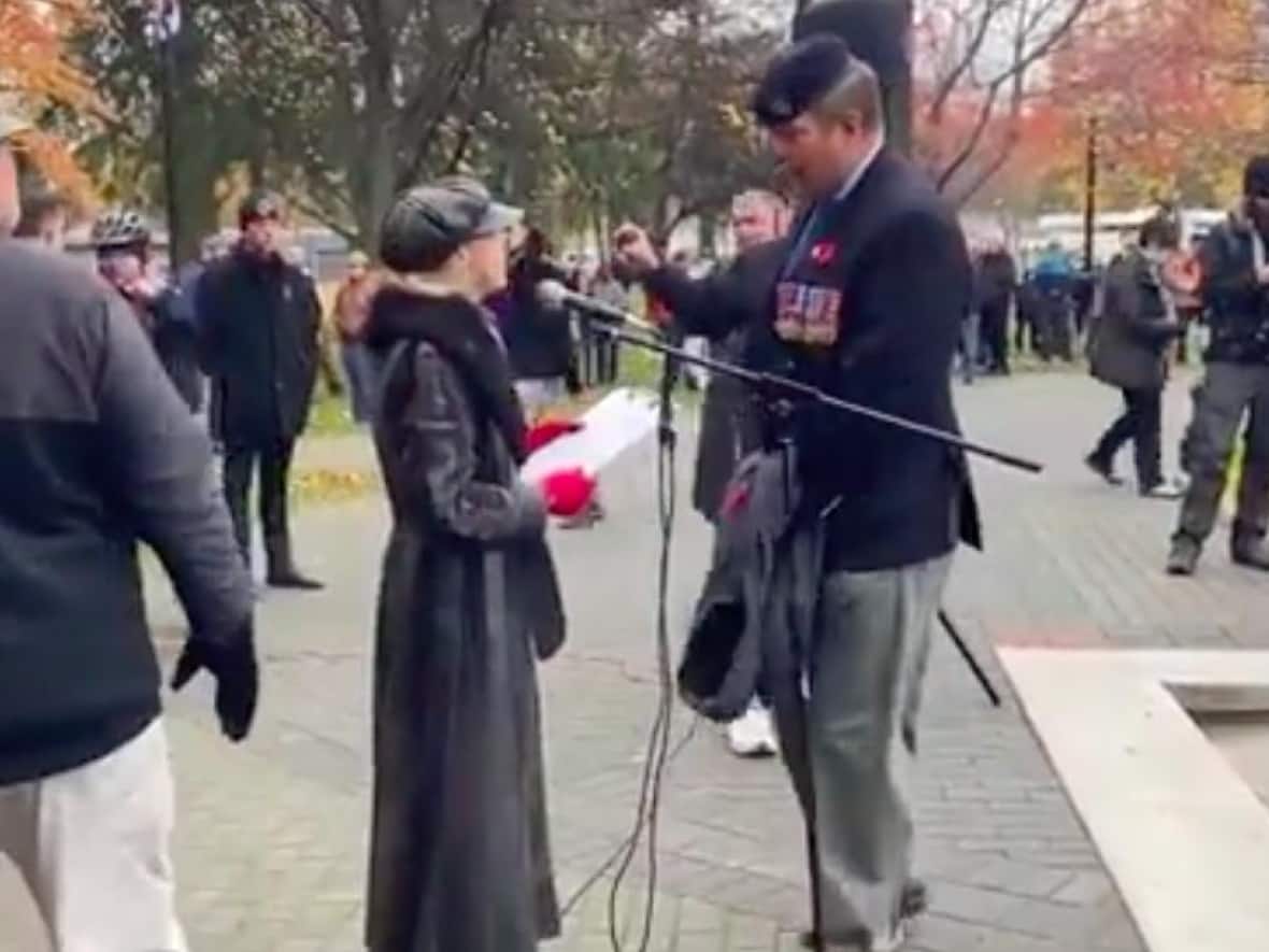 A still from a video shows a demonstrator protesting against COVID-19 vaccine mandates at a Remembrance Day ceremony in Kelowna, B.C., being confronted by several onlookers. (Courtesy of Kelowna Now - image credit)