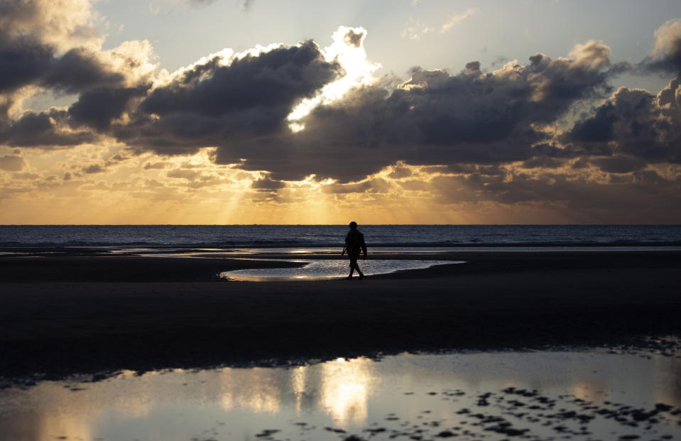 A man in a vintage US WWII uniform walks at sunrise prior to a D-Day 76th anniversary ceremony in Saint Laurent sur Mer, Normandy, France, Saturday, June 6, 2020. Due to coronavirus measures many ceremonies and memorials have been cancelled in the region with the exception of very small gatherings. (AP Photo/Virginia Mayo)