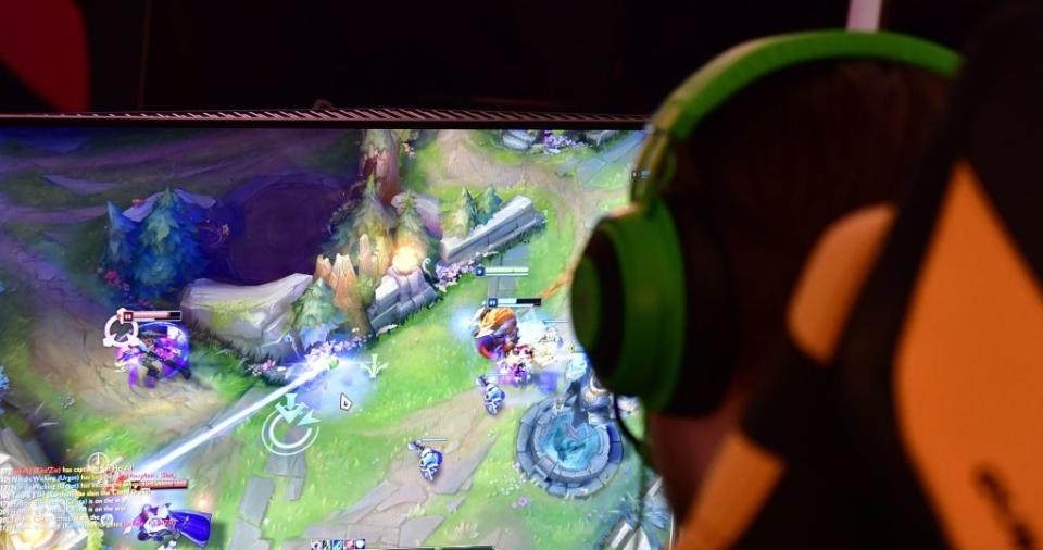 A person wearing green headphones plays the popular video game "League of Legends." The screen displays an ongoing match with multiple characters in action