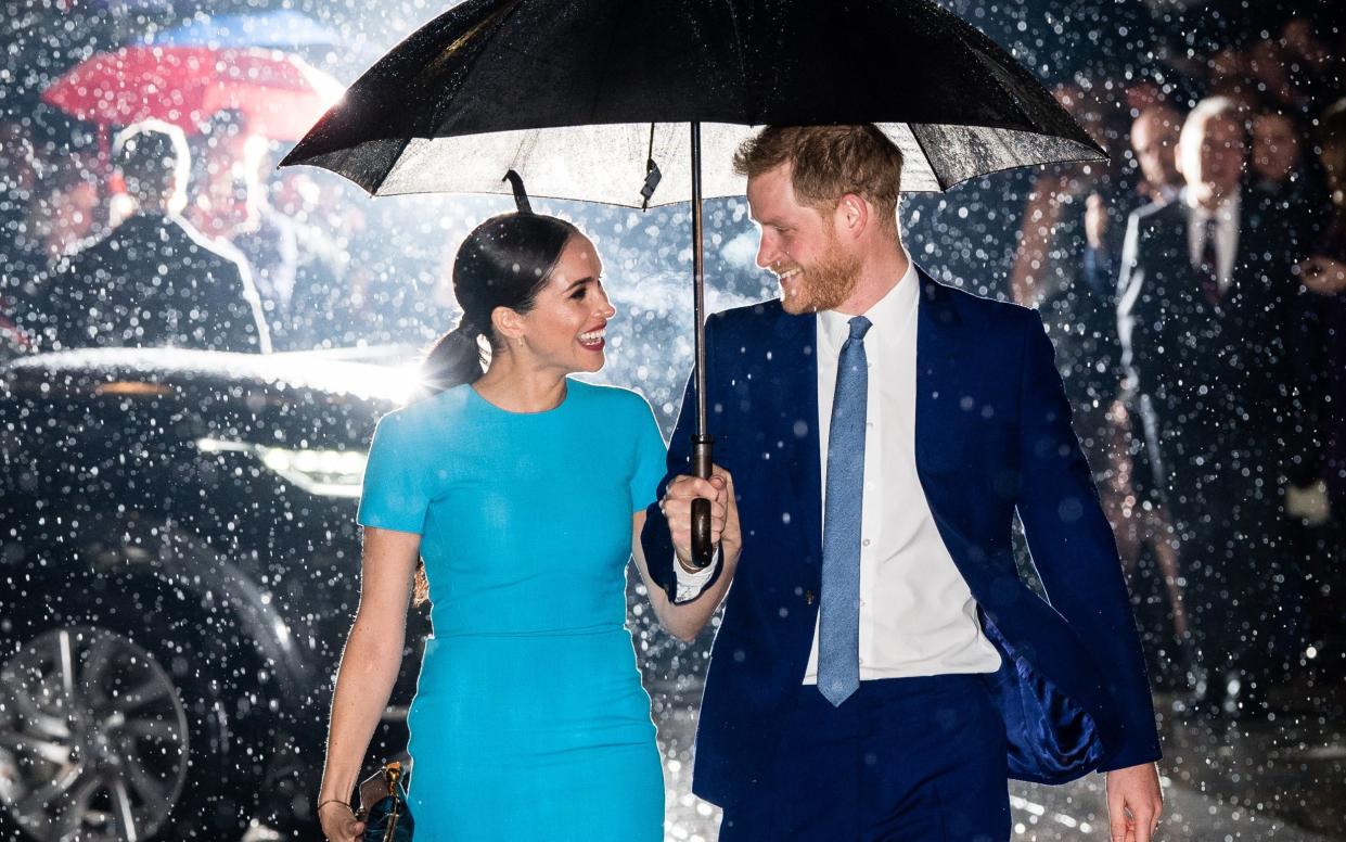 The Duke and Duchess of Sussex shelter under an umbrella in London