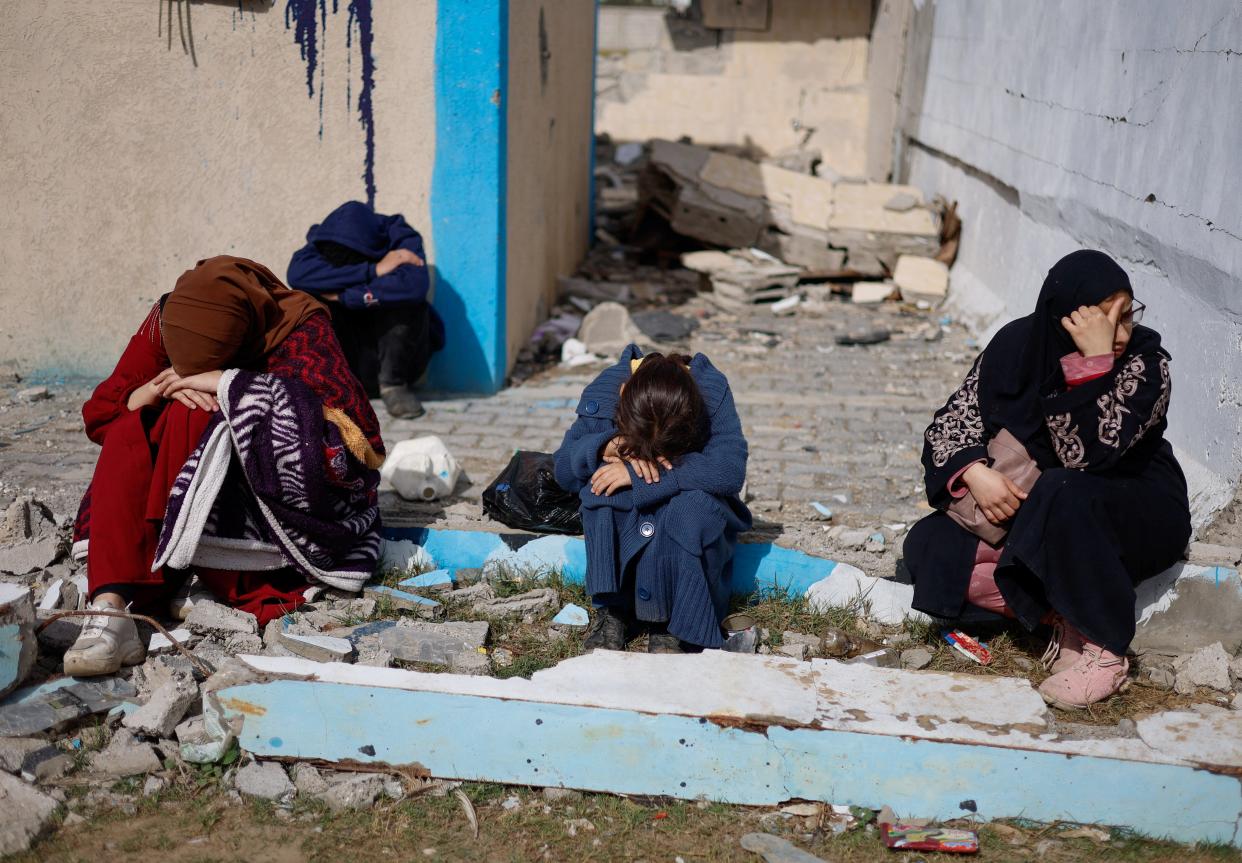 People rest next to damaged buildings, as Palestinian arrive in Rafah after they were evacuated from Nasser hospital in Khan Younis due to the Israeli ground operation, amid the ongoing conflict between Israel and Hamas, in the southern Gaza Strip, 15 February 2024 (REUTERS)