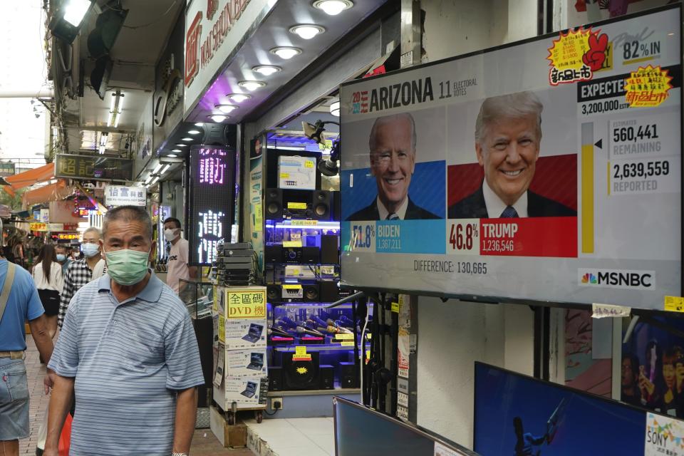 A man walks past a TV monitor showing a news program reporting the U.S. presidential election between President Donald Trump, right, and former Vice President Joe Biden, left, in Hong Kong, Wednesday, Nov. 4, 2020. ( AP Photo/Kin Cheung)