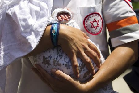 An Israeli medic holds a baby, born to a surrogate mother, who was evacuated from Nepal and landed at Ben Gurion international airport near Tel Aviv, Israel April 28, 2015. REUTERS/Amir Cohen