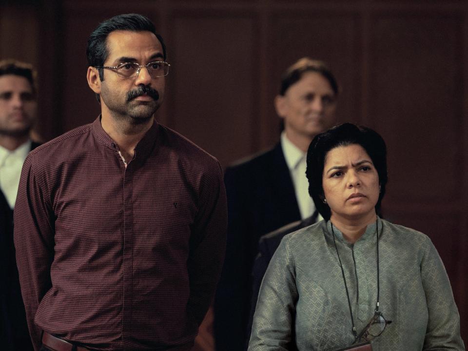 a man and woman in trial by fire, looking concerned and standing together in what appears to be a courtroom