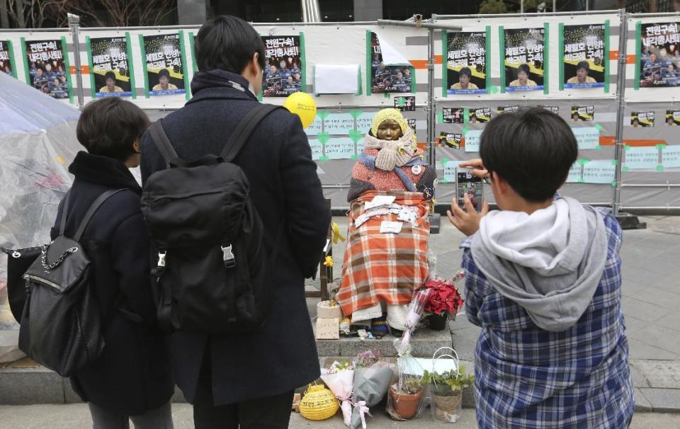 People watch a statue symbolizing women forced into wartime Japanese military brothels in front of the Japanese Embassy in Seoul, South Korea, Sunday, Jan. 8, 2017. A South Korean Buddhist monk is in critical condition after setting himself on fire to protest the country's settlement with Japan on compensation for wartime sex slaves, officials said Sunday. (AP Photo/Ahn Young-joon)