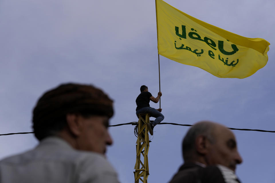 A Hezbollah supporter sits on an electricity column, as he waves a flag with Hezbollah electoral slogans that read: We will stay protect and build," during an election campaign, in Baalbek, east Lebanon, Friday, May 13, 2022. Despite a devastating economic collapse and multiple other crises gripping Lebanon, the culmination of decades of corruption and mismanagement, the deeply divisive issue of Hezbollah's weapons has been at the center of Sunday's vote for a new 128-member parliament. (AP Photo/Hussein Malla)