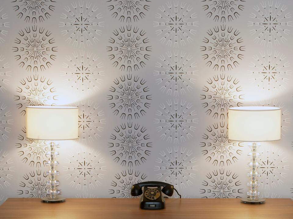 Wooden desk and chair with telephone centered on top and two matching lamps in front of lavender and brown patterned wallpaper