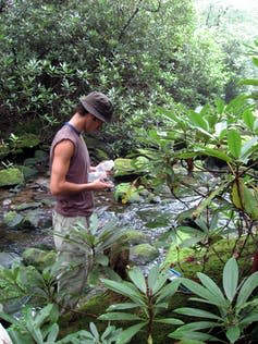 Man holding plastic bottles stands in stream.