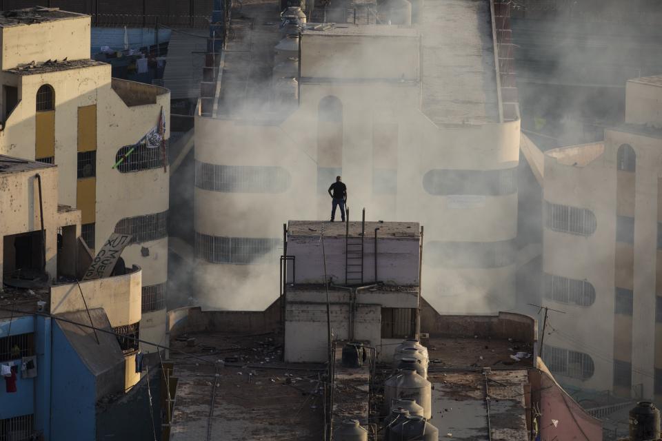 A police officer stands on the roof during a prison riot at Castro Castro prison in Lima, Peru, Monday, April 27, 2020. Peru's prison agency reported that three prisoners died from causes still under investigation after a riot at the Miguel Castro Castro prison in Lima. Inmates complain authorities are not doing enough to prevent the spread of coronavirus inside the prison. (AP Photo/Rodrigo Abd)