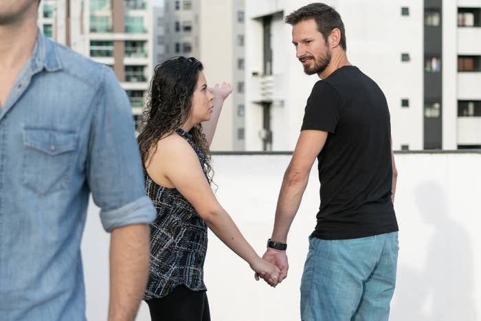 A guy checks out another man while holding his girlfriend's hand