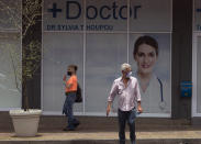 Pedestrians wearing masks to protect against coronavirus pass a sign for doctors rooms in Johannesburg Tuesday, Dec. 29, 2020. South African President Cyril Ramaphosa has declared the wearing of masks compulsory and has reimposed a ban on the sales of alcohol and ordered the closure of all bars as part of new restrictions to help the country battle a resurgence of the coronavirus, including a new variant. (AP Photo/Denis Farrell)