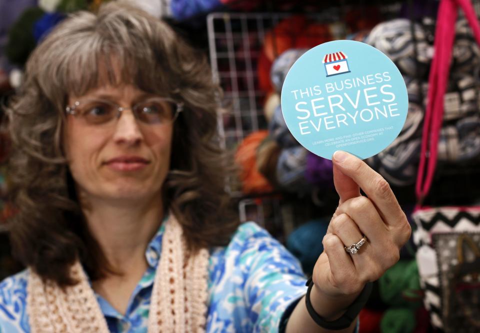 Elizabeth Ladd, owner of River Knits Fine Yarns, poses while holding up a "This businesses serves everyone" sticker she plans to place outside her business in downtown Lafayette, Indiana March 31, 2015. Indiana's Republican Governor Mike Pence, responding to national outrage over the state's new Religious Freedom Restoration Act, said on Tuesday he will "fix" it to make clear businesses cannot use the law to deny services to same-sex couples. (REUTERS/Nate Chute)