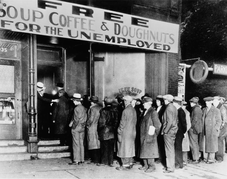 men in suits and coats stand in line under a sign that says "free soup coffee & doughnuts for the unemployed"