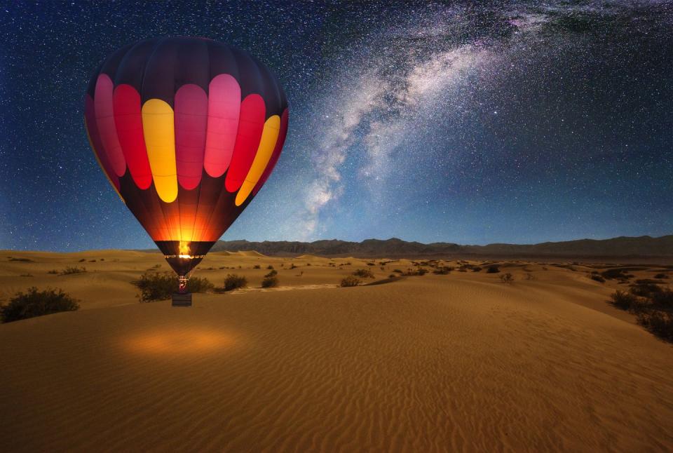 a majestic hot air balloon soars under the stars of the milky way, over the desert mesquite dunes of death valley national park moonlight provides luminosity showing the patterns and shapes of the desert landscape