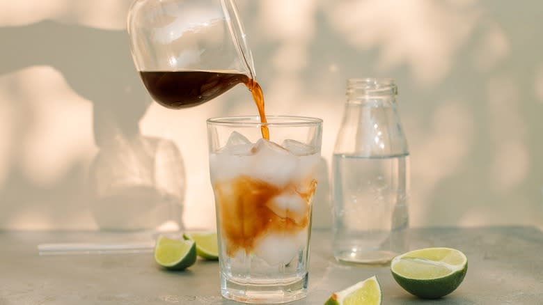 Coffee being poured into a glass with ice and limes