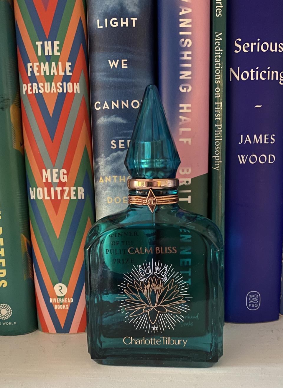 a bottle of charlotte tilbury perfume sitting in front of a shelf of multicolor books