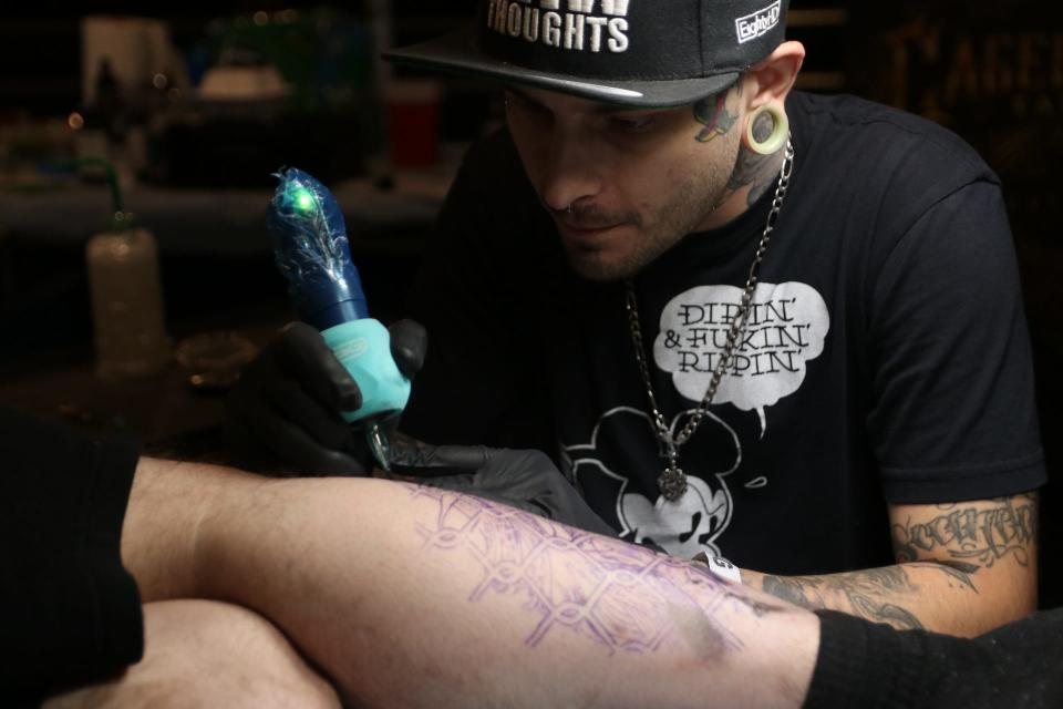Sean Cutthroat of Caged Raven Tattoo works on a customer at the Tattoo the Earth festival Saturday in Worcester.
