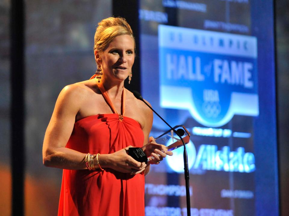 Jenny Thompson on stage today wearing a red dress and holding a trophy.