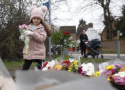 A young girl lays a floral tribute to Captain Tom Moore in Marston Moretaine, England, Wednesday, Feb. 3, 2021. Captain Tom Moore, the 100-year-old World War II veteran who captivated the British public in the early days of the coronavirus pandemic with his fundraising efforts for medical care workers, died Tuesday. (AP Photo/Alastair Grant)