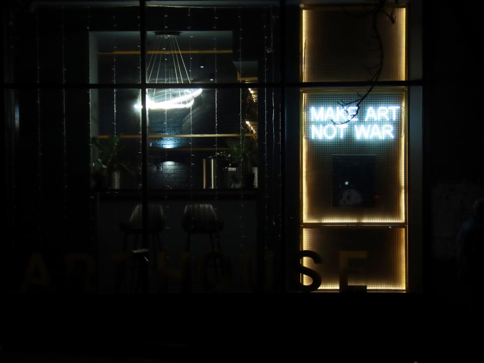 A dark window with a lit-up sign that says "Make Art Not War"