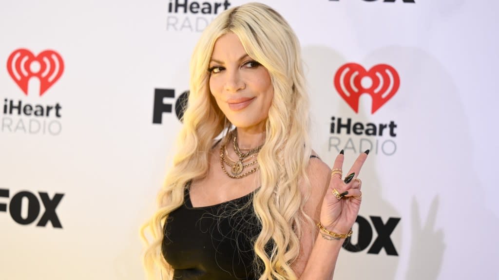 Tori Spelling posing in a black dress and holding up the peace sign