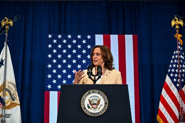 La vicepresidenta Kamala Harris al micrófono con una bandera estadounidense detrás y el sello del vicepresidente en el podio.