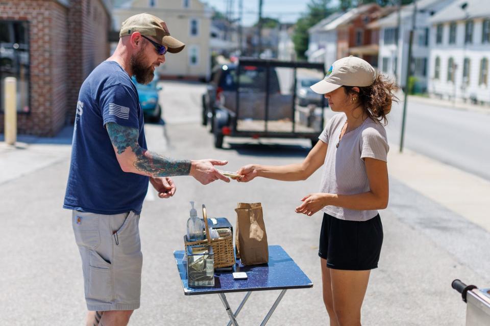 Juli Madrigal hands an order to a customer at The Homedog LLC hot dog cart in the WE Sell Sporting Goods parking lot at the corner of Pleasant and York Streets, Tuesday, May 21, 2024, in Hanover Borough.