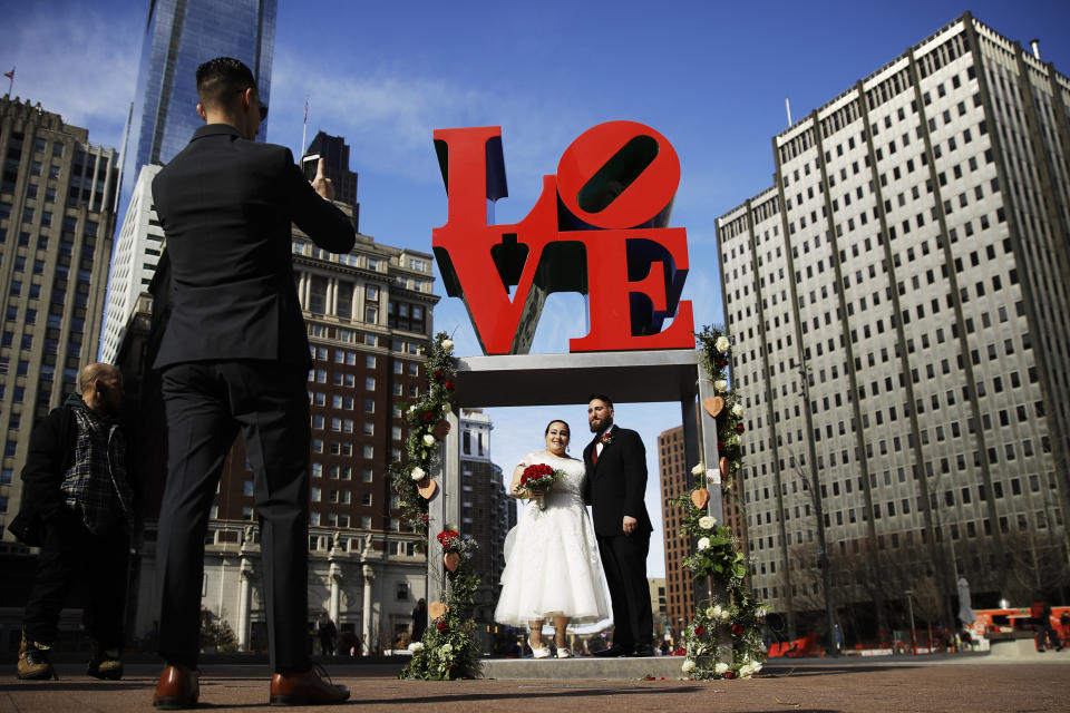 FILE - In this Feb. 14, 2019 file photo, newlyweds Jennifer and Paul Raffa pose for a photograph under the Robert Indiana "LOVE" sculpture at John F. Kennedy Plaza in Philadelphia on Valentine's Day. Indiana's estate has reached a settlement that keeps intact a longstanding relationship with the copyright holder of the iconic "LOVE" series. Officials said Friday, June 11, 2021, that New York-based Morgan Art Foundation will work with the Maine-based Star of Hope Foundation, which aims to transform Indiana's island home in Maine into a museum. (AP Photo/Matt Rourke, File)