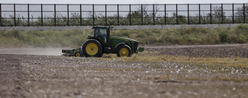 In this Sept. 6, 2012, photo, a tractor is used to farm in cotton field along a border fence that passes through the property in Brownsville, Texas. Since 2008, hundreds of landowners on the U.S.-Mexico border have sought fair prices for property that was condemned to make way for the fence, but many of them received initial offers that were far below market value. (AP Photo/Eric Gay)