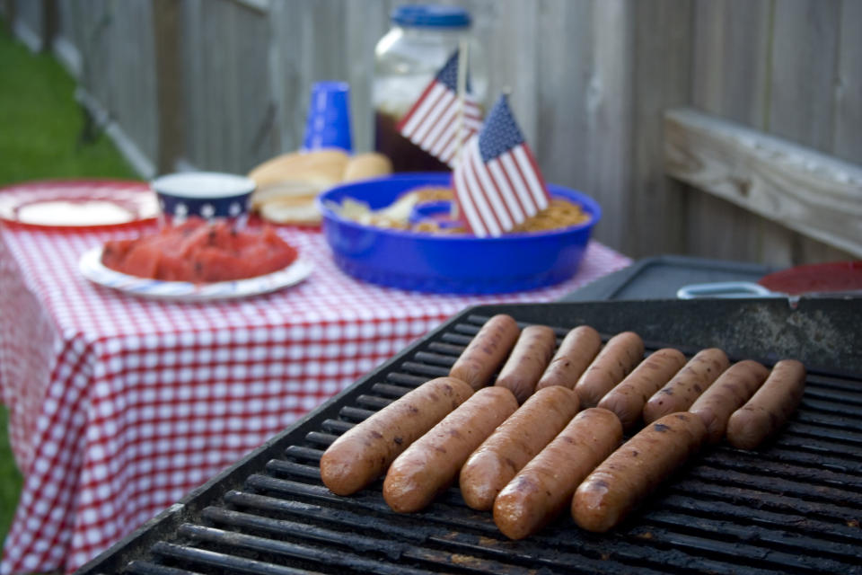 Hot dogs on the grill with a festive red, white and blue table in the background, complete with watermelon and a pot of sweet tea! Nothing is more American... Happy Independence Day!